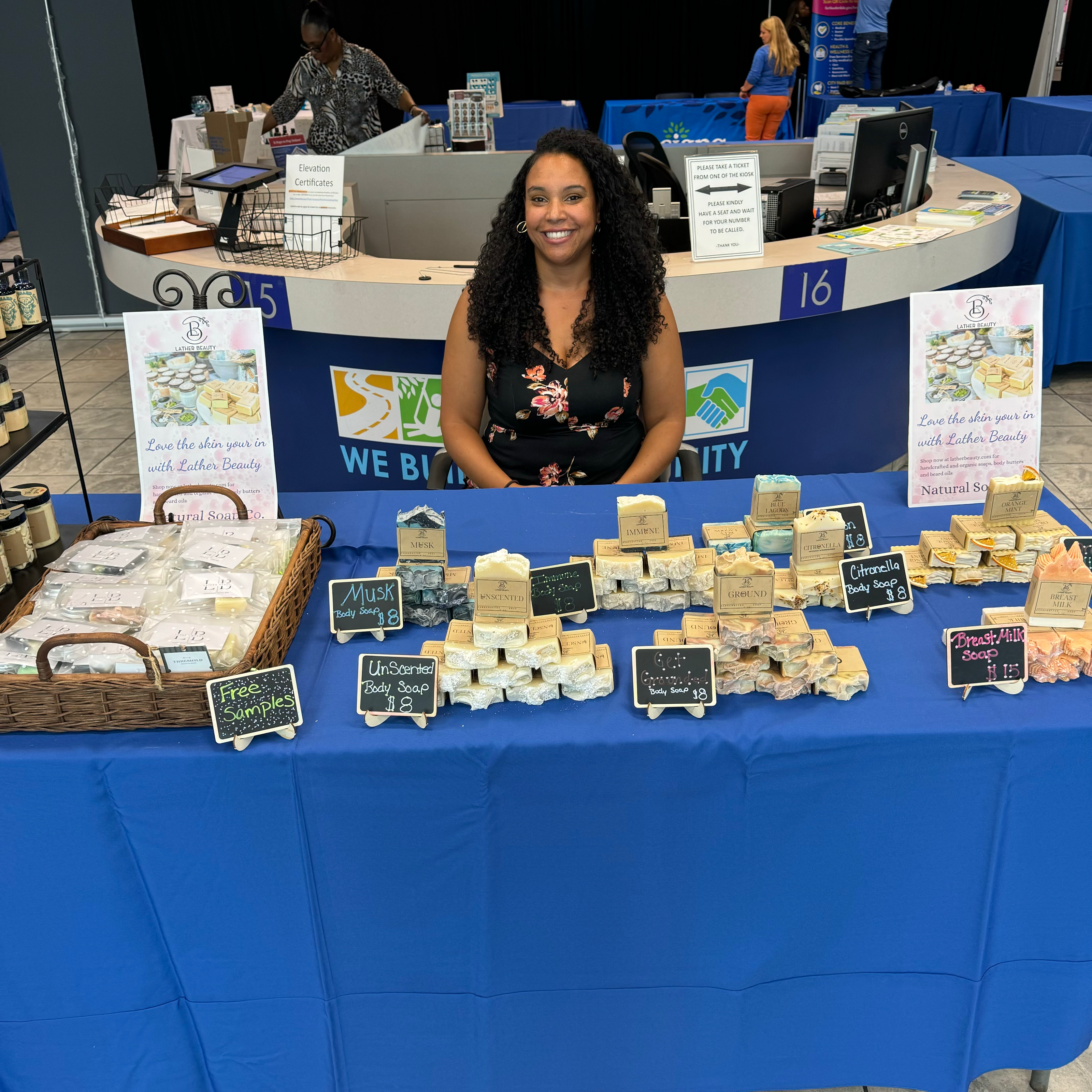 Female owner smiling Lather Beauty at pop event with a blue cover and organic soaps